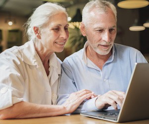 Pareja de adultos mayores revisando la laptop que está sobre la mesa