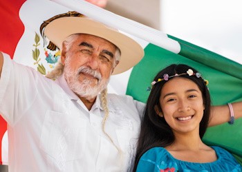 Adulto mayor sostiene la bandera de México y frente a él hay una niña sonriendo