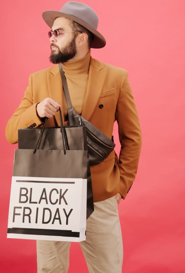 Un garçon sur fond rose faisant du shopping le jour du Black Friday : profitez des codes promo sur bravopromo.fr pour la Black Week