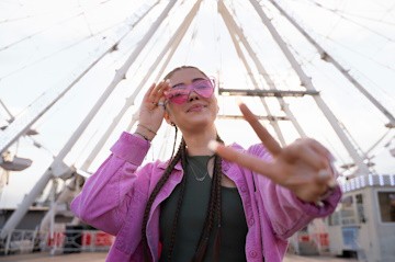 Chica con trenzas y gafas de sol frente a una noria