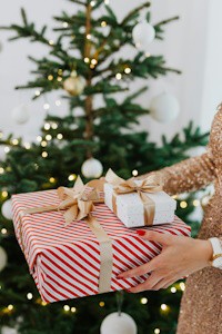 Una mujer sostiene un regalo envuelto de papel blanco frente a un árbol de navidad