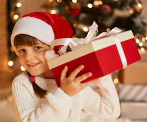 Niña sonriente con un gorro de Santa Claus sostiene un regalo navideño en las manos