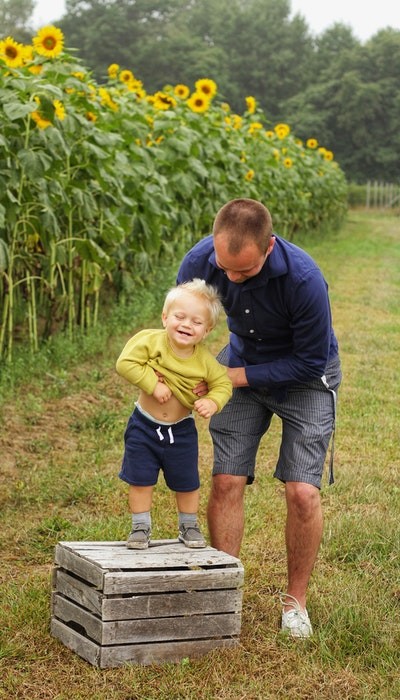 Père avec son bébé dans un champ de tournesols en train de jouer : trouvez des codes de réduction pour bébés sur bravopromo.fr