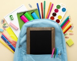 mochila azul con útiles escolares que sobresalen de ella y una pizarra enfrente