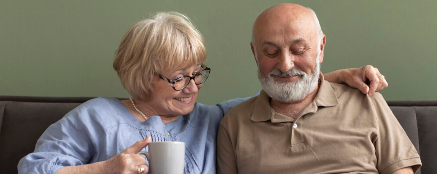 Señor y señora mayor, sentados en un sofá sonriendo y mirando información