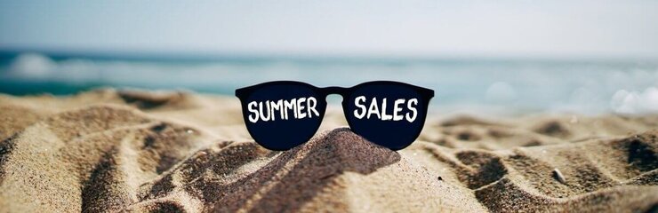 Gafas de sol apoyadas en la arena de la playa con el escrito "Summer sales"