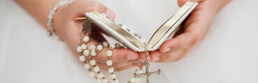 Manos de niño/a sujetando un rosario y la biblia