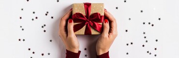 Manos de mujer sosteniendo caja de regalo con lazo rojo y estrellas de decoración