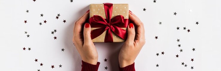 Manos de mujer sosteniendo caja de regalo con lazo rojo y estrellas de decoración