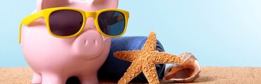 Alcancía con forma de cerdito rosa, con gafas de sol amarillas sobre la arena de la playa, con toalla, estrella y concha de mar
