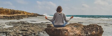 Chica sentada en una roca frente al mar en posición de meditación