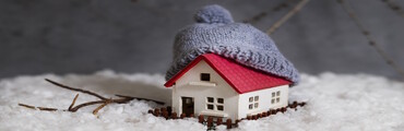 Maqueta de casita pequeña rodeada de nieve y decorada con un gorro en el tejado