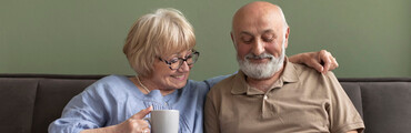 Señor y señora mayor, sentados en un sofá sonriendo y mirando información