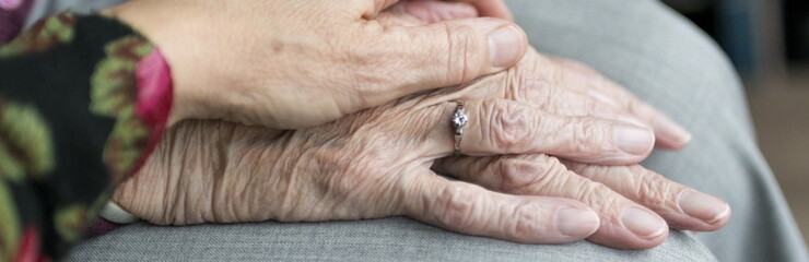 Mano de persona joven apoyada sobre las manos de persona anciana