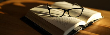 Libro abierto apoyado sobre una mesa con unas gafas de leer encima