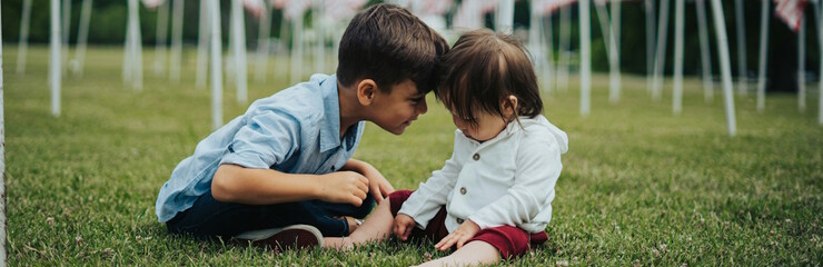 Dos niños pequeños, probablemente hermanos, sentados en la hierba y unidos frente a frente