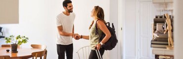 un host (proprietario o gestore) e un inquilino temporaneo (ospite) si scambiano una stretta di mano amichevole all'interno di un appartamento arredato, simbolo di benvenuto e inizio di un soggiorno