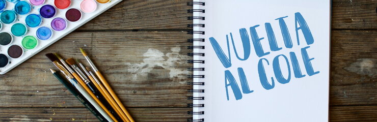 Cuaderno con portada donde pone "Vuelta al cole" junto a pinceles y colores