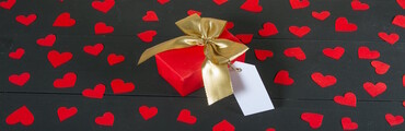 Ein Geschenk mit Schleife und Namensschild auf schwarzem Untergrund mit Herzen