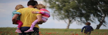 ein Vater in einem Feld, der zwei Kinder auf dem Arm trägt