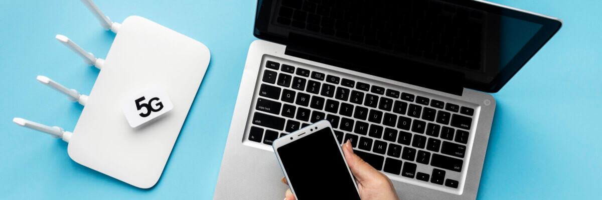 Portátil sobre una mesa, con aparato wifi 5G y celular de chica