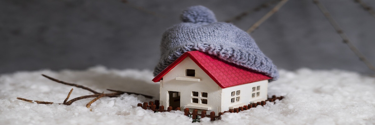Maqueta de casita pequeña rodeada de nieve y decorada con un gorro en el tejado