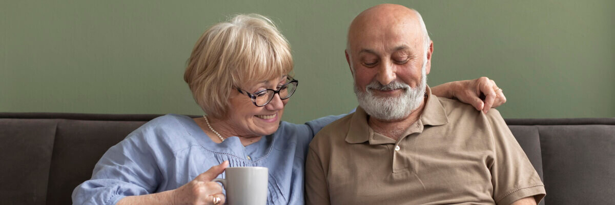 Señor y señora mayor, sentados en un sofá sonriendo y mirando información