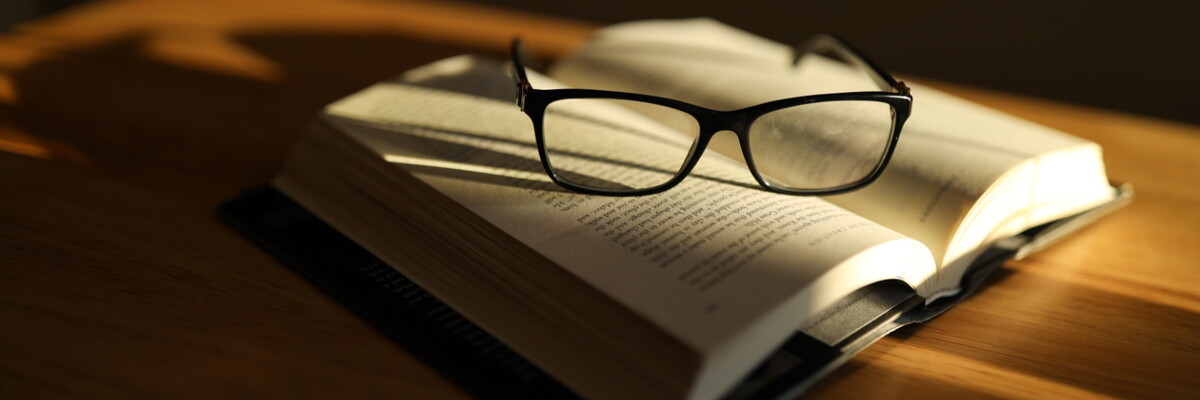 Libro abierto apoyado sobre una mesa con unas gafas de leer encima