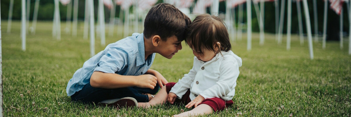 Dos niños pequeños, probablemente hermanos, sentados en la hierba y unidos frente a frente