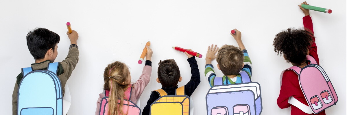 Cinco niños de espaldas cargando sus mochilas y dibujando en una pared blanca con colores