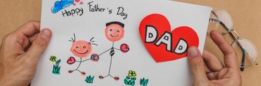 Manos de hombre sujetando un dibujo con una decicatoria deseando " Feliz día del padre"