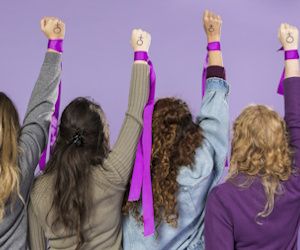 fondo lila con 4 mujeres de espalda que alzan su brazo con un lazo lila y el simbolo femenino dibujado en sus manos