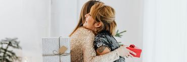Duas mulheres a abraçarem-se e a oferecerem presentes uma à outra no Natal