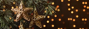 Estrellas colgando de árbol de Navidad con luces en el fondo