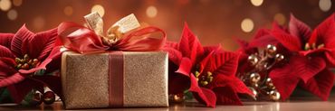 caja de regalo color oro cerrada con lazo rojo con flores rojas de navidad y luces alrededor