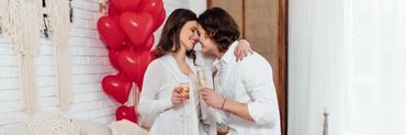 Pareja abrazada encima de una cama rodeados de decoración de San Valentín