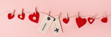 Fondo rosa con corazones de papel rojos sujetados por pinzas de madera con el numero 14 en medio de ellos