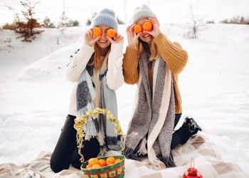 Aprovecha las rebajas en comida de temporada Dos chicas en la nieve con una cesta de naranjas y dos naranjas en sus ojos