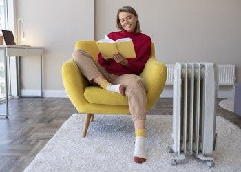 Aprovecha las rebajas en calefacción Chica sentada leyendo un libro con estufa al lado