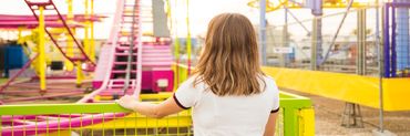 petite fille blonde de dos regardant une aire de jeux devant elle
