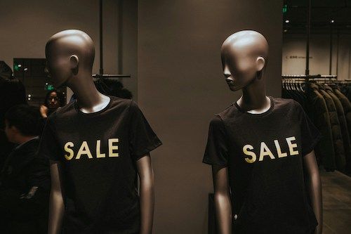 Dois manequins numa loja com t-shirts pretas com a palavra “Sale”.
