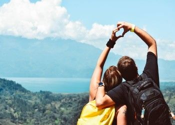 Pareja encima de una montaña viendo la vista y haciendo forma de corazón con sus brazos Escapadas de San Valentín