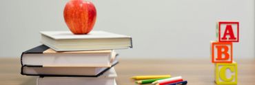 mesa con libros apilados, una manzana, colores y unos cubos con el ABC